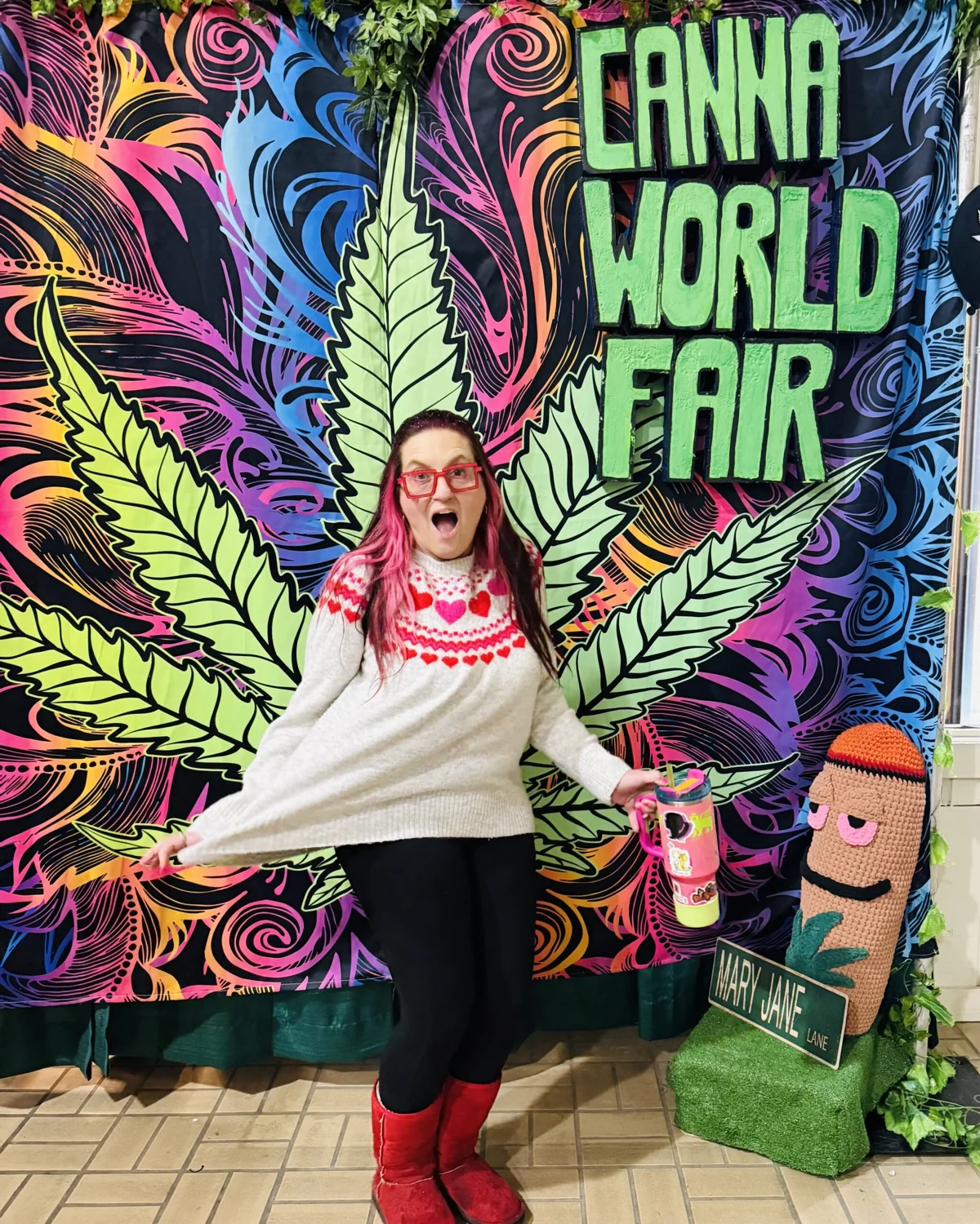 A fair attendee poses in front of a colorful Canna World Fair backdrop